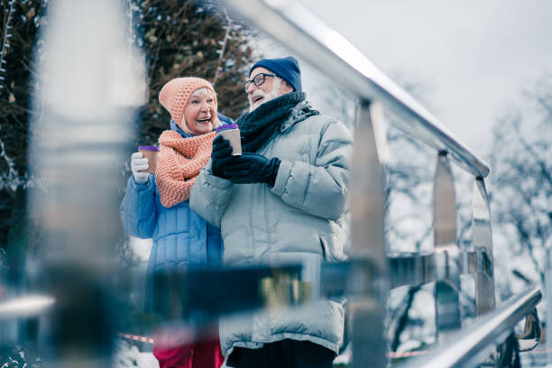 Cheerful elderly people walking with hot chocolate in paper cups and smiling while enjoying winter day outdoors